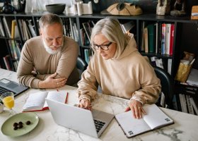 A senior couple working with laptops and paper notebooks